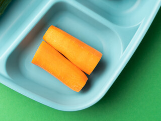 Carrot lie on a plastic plate. Healthy food, green background. Close up, top shot, copy space, nobody.
