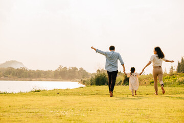 Back of Asian family enjoying a morning walk in a beautiful park, with green fields and a sunny...