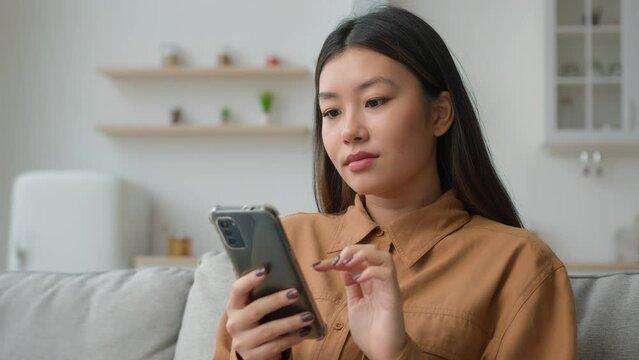 Korean chinese multiracial woman use smartphone application surfing internet social media pensive Asian housewife girl in kitchen typing mobile phone message buy goods online order delivery at home