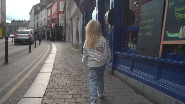 A cute little girl strolls down an old town street in Ireland. Spring 2023