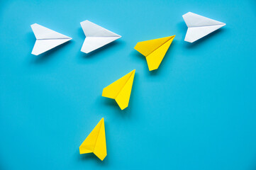 Yellow paper airplane origami joining other white airplanes on blue background with customizable space for text or ideas. Leadership concept.