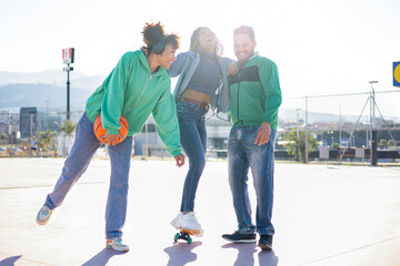 A group of happy and diverse friends gather on a basketball court. The boys on the sides help the black girl with braids learn to skate. Concept of social relations between different ethnic groups.