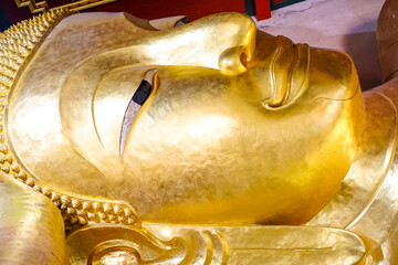The close up face of the Reclining Buddha statue image at Wat Phra Phut Saiyat or Saiyat Buddhist temple in Phetchaburi province, Thailand.