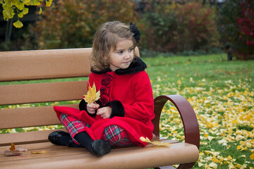Cute little girl wearing red sitting on the bench in an autumn park