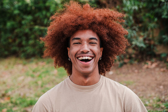 Close up portrait of young african american toothy man with afro hair smiling looking at camera outdoors. Head shot of a glad teenager boy laughing with friendly and carefree attitude. High quality