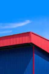 Blue corrugated steel wall with red roof of warehouse building against blue sky background in vertical frame