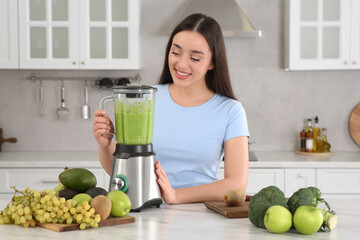 Beautiful young woman preparing tasty smoothie at white table in kitchen