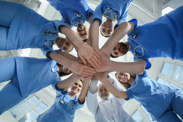 Doctor and interns stacking hands together indoors, bottom view