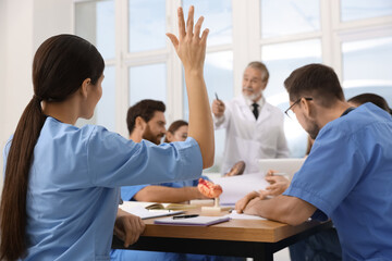 Intern raising hand to ask doctor question at lecture in hospital - obrazy, fototapety, plakaty