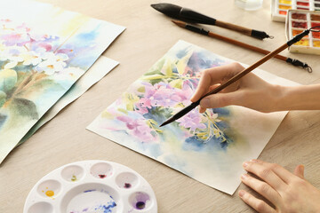 Woman painting flowers with watercolor at white wooden table, closeup. Creative artwork