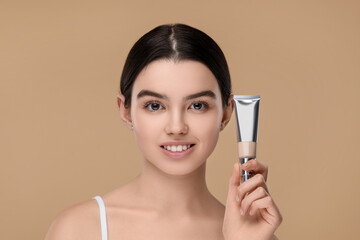 Fototapeta premium Teenage girl holding tube with foundation on beige background