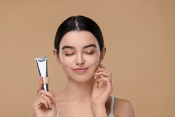 Teenage girl holding tube with foundation on beige background