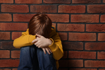 Upset boy sitting near brick wall. Children's bullying