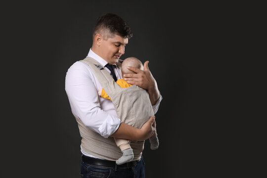 Father holding his child in baby carrier on black background. Space for text