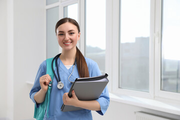 Smart medical student with folders in college hallway, space for text