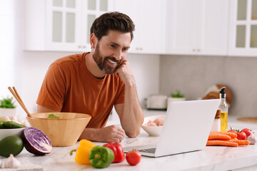 Man making dinner while watching online cooking course via laptop in kitchen