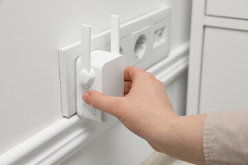 Woman turning on wireless Wi-Fi repeater indoors, closeup