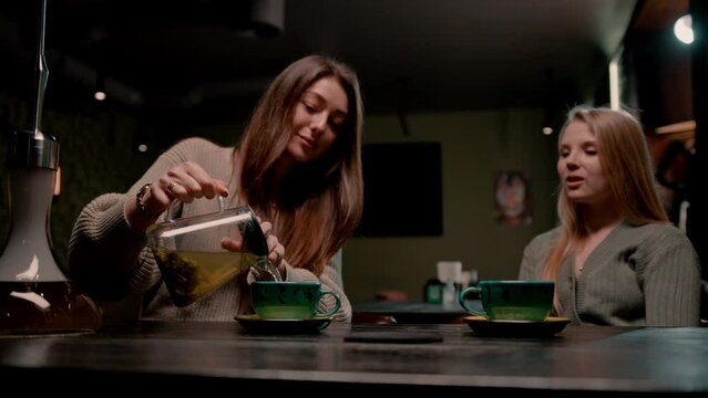 A girl pours hot tea from a teapot into a cup while sitting in a hookah the concept of relaxation