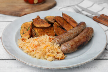 Plate with sauerkraut, sausages and potatoes on white wooden table, closeup