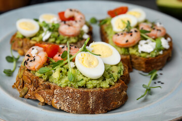 Delicious sandwiches with guacamole, shrimps and eggs on plate, closeup