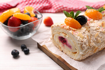 Tasty meringue roll with jam, tangerine slices and mint leaves on white wooden table, closeup