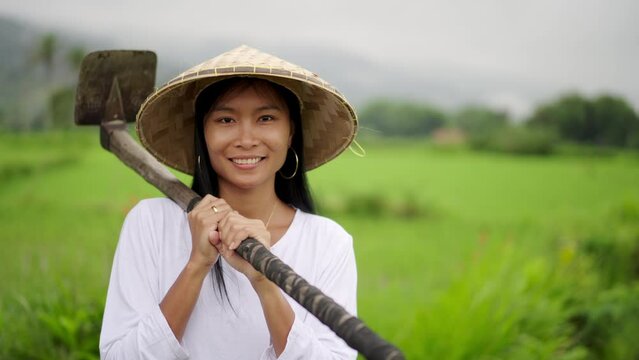 Happy female smallholder joyfully smiling, rice paddy field in background, crop