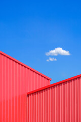 Two red Corrugated metal walls of Warehouse Building interlock in geometric shape against blue sky...