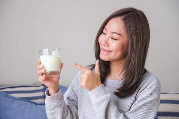 Portrait image of a young woman holding and pointing finger at a glass of fresh milk