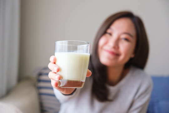Blurred image of a young woman holding and showing a glass of fresh milk