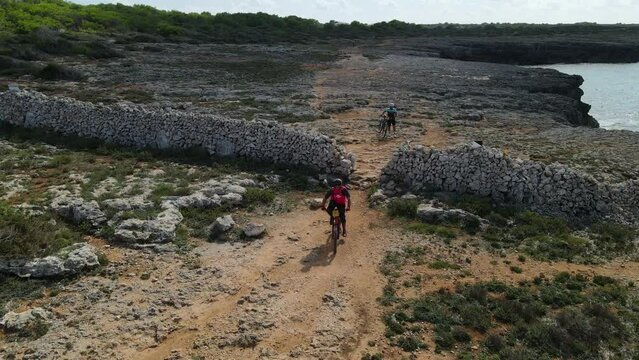 Close up drone of 3 bike riders crossing stone wall and 1 rider walking bike over.