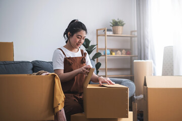 New house, asian woman sealed box while feeling proud and excited about buying a house with a mortgage loan. Young asian woman first time buyers unpacking in dream home or apartment