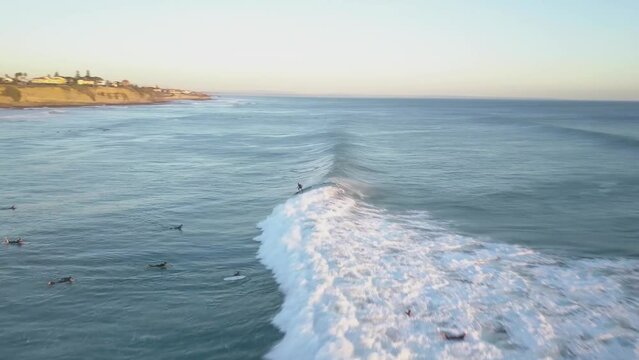 Drone flight following a surfer on waves into sand beach in Estoril, Cascais. People caching some sun on beach.