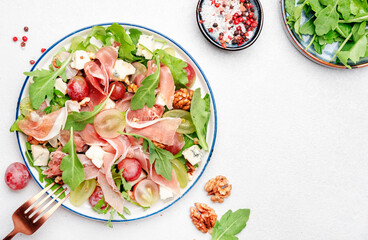 Fresh grape salad with jamon, blue cheese, arugula, nuts on white table background, top view, copy space
