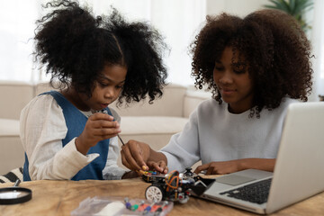African American female and child girl building automatic toy car technology from online laptop computer. Teacher and child girl learning checking, repairing robotics toy car from online - Powered by Adobe