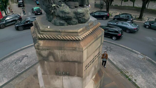 Tourist admiring Pedro &Aacute;lvares Cabral statue, viewed from below against a backdrop of cloudy sky. Aerial perspective adds a unique dimension. Urban and city life.