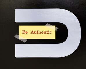 U letter on black wall with note written BE AUTHENTIC, concept of being true authentic self,...