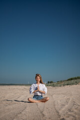Fototapeta na wymiar Girl meditating by the sea. Wind shakes long blond hair