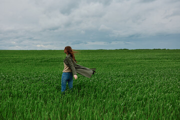 a woman in a dark coat walks through a field with tall grass in windy, rainy weather