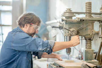 Carpenter uses drilling machine to make a hole on wooden plank