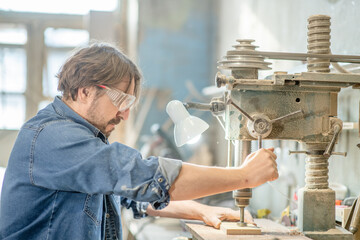 Craftsman uses drilling machine to make a hole on wooden plank