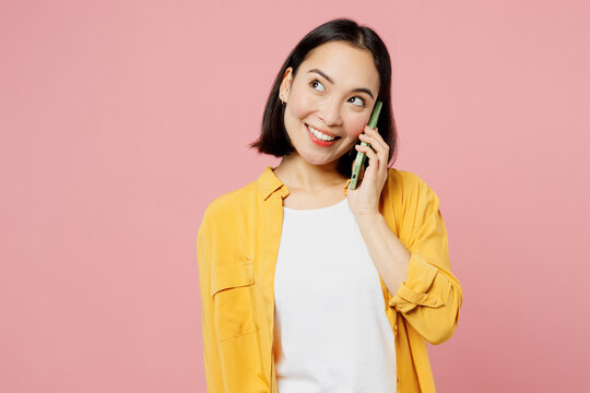 Young woman of Asian ethnicity wear yellow shirt white t-shirt talk speak on mobile cell phone conducting pleasant conversation isolated on plain pastel light pink background studio Lifestyle concept.
