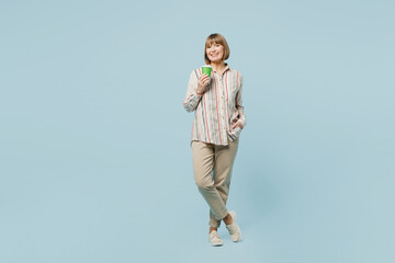 Full body elderly woman 50s years old wear shirt hold takeaway delivery craft paper brown cup coffee to go isolated on plain pastel light blue cyan color background studio portrait. Lifestyle concept.