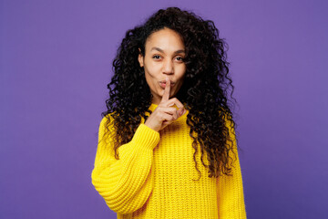 Young secret woman of African American ethnicity wear casual yellow sweater say hush be quiet with...