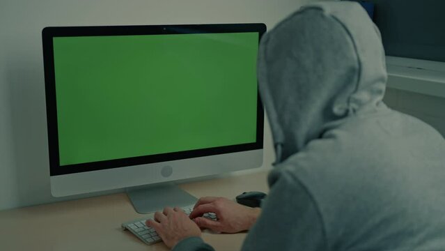 man wearing gray hood typing on keyboard using pc display with green screen minimalist workplace at home or office