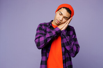 Young calm tranquil happy man of African American ethnicity wearing casual shirt orange hat sleep with folded hands under cheek isolated on plain pastel light purple color background studio portrait.