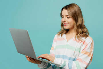 Side view young IT woman wear striped hoody hold use work on laptop pc computer chatting online browsing internet isolated on plain pastel light blue cyan background studio portrait Lifestyle concept