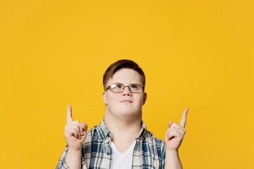 Young man with down syndrome wears glasses casual clothes point index finger overhead on area...