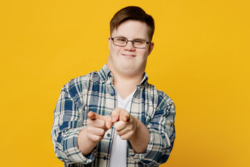 Young smiling man with down syndrome wearing glasses casual clothes point index finger camera on you motivating encourage isolated on plain yellow color background. Genetic disease world day concept.