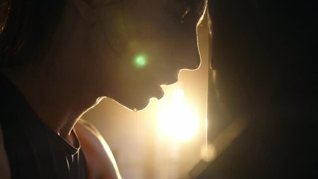 Silhouette face of young tired exhausted sportswoman boxer loaning head to punching bag, side view. Sweaty girl is resting after workout. Training box, practicing fight, professional sport concept.