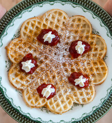  A garnished waffle lies on a green 50s plate and a Gröna Anna plate. On the waffle there is strawberry jam and split cream
